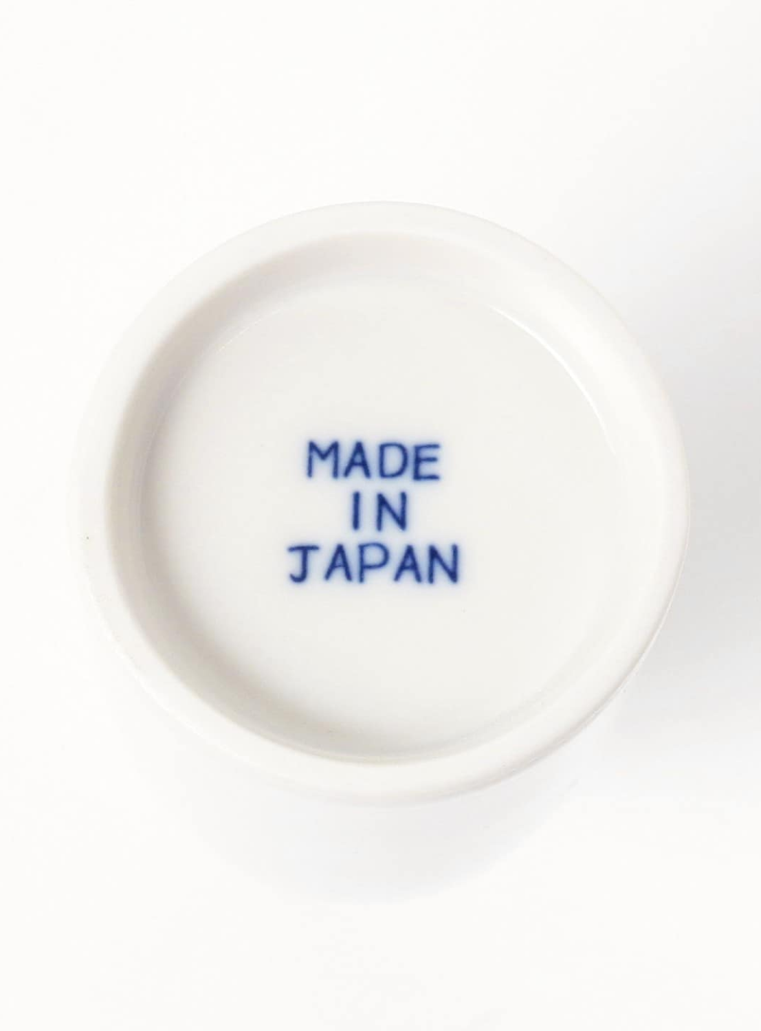 A white ceramic dish with MADE IN JAPAN printed in bold blue capital letters at the center, ideal for pairing with your BEAMS JAPAN Sake Bottle 360ML or other traditional sake ware from BEAMS JAPAN.