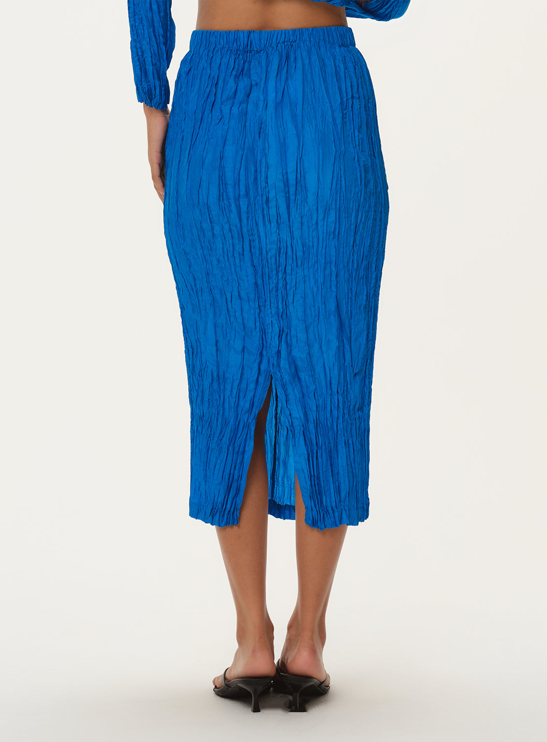 Back view of a model wearing a blue pleated midi skirt with a back slit.