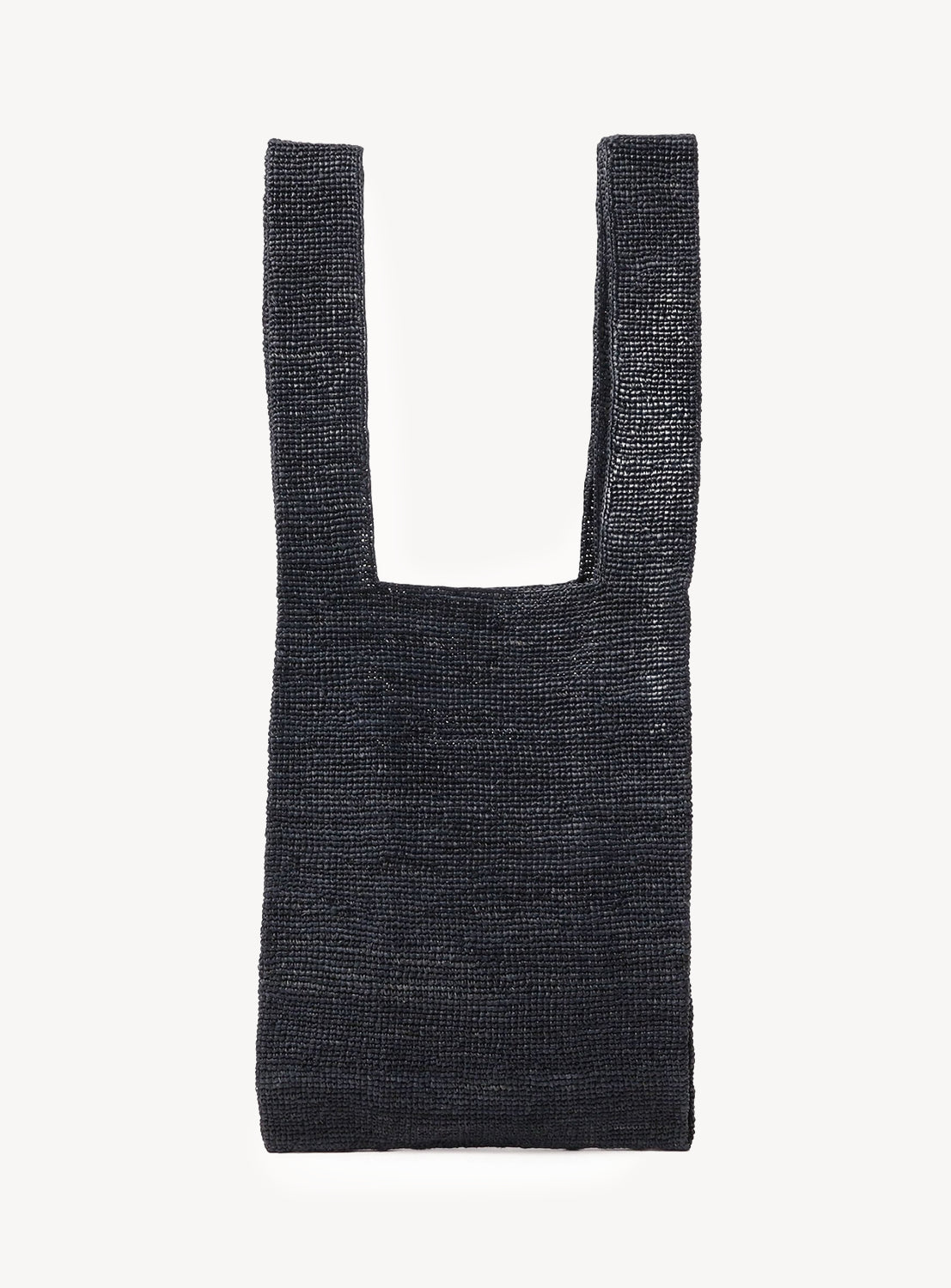 The Raffia Shopper Bag by seya. is a black, rectangular, handcrafted accessory with wide flat handles and a textured woven pattern, displayed against a plain white background and inspired by traditional Madagascar bags.