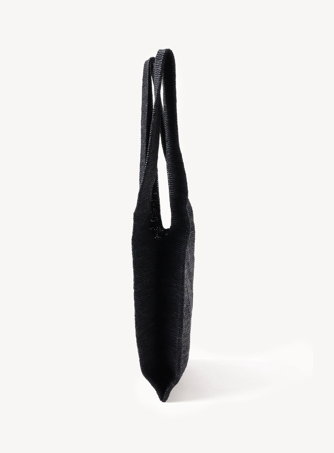 The Raffia Shopper Bag by seya., shown upright from the side on a white background, features black handwoven raffia and two shoulder straps.