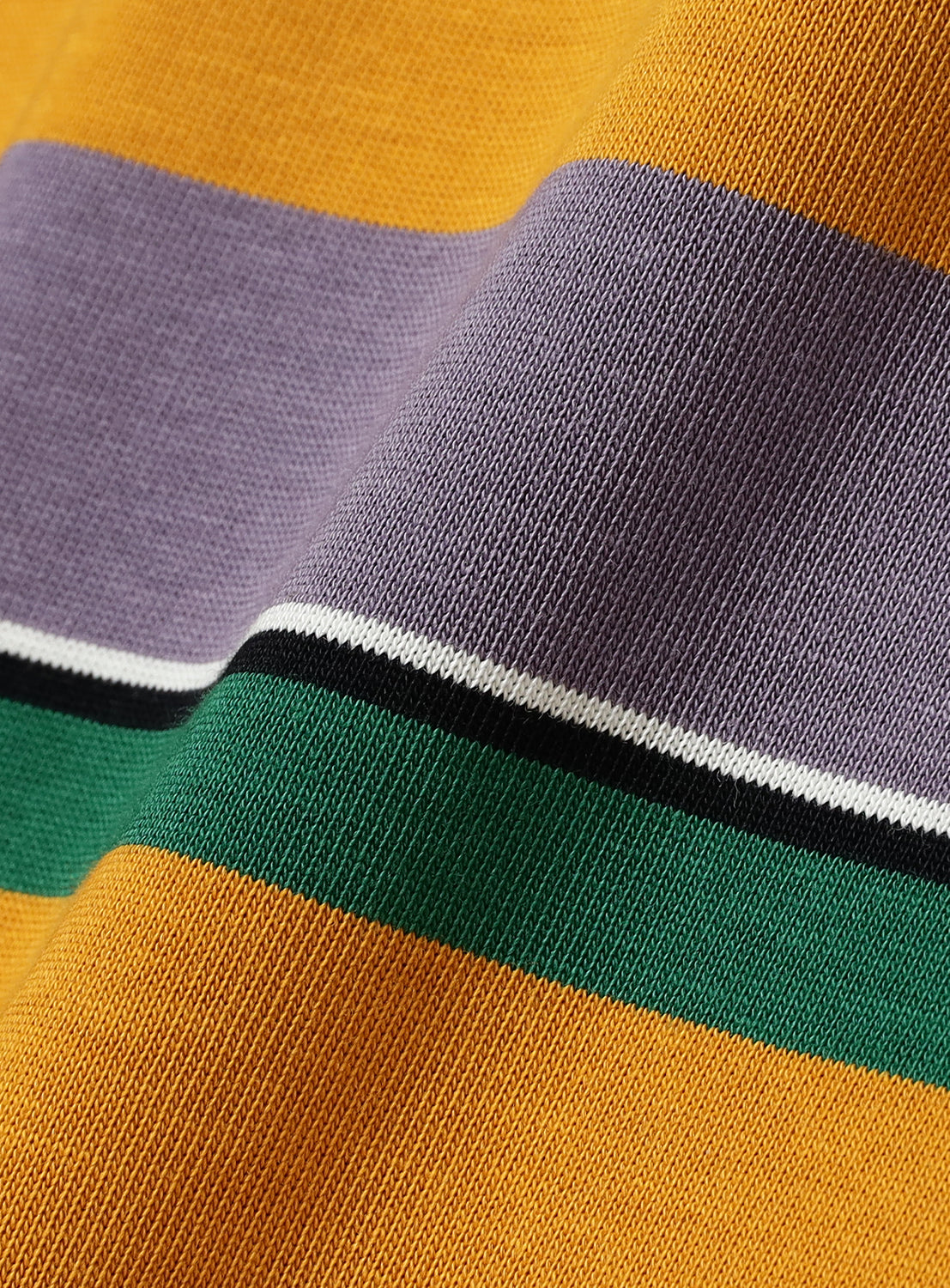Close-up of the BEAMS Multi-Border T-Shirt showcasing its 100% cotton fabric with horizontal stripes in mustard yellow, lavender, white, black, and green. The knitted texture and gentle folds emphasize the soft comfort of this crewneck tee, while the multi-colored border stripes highlight its distinctive design.