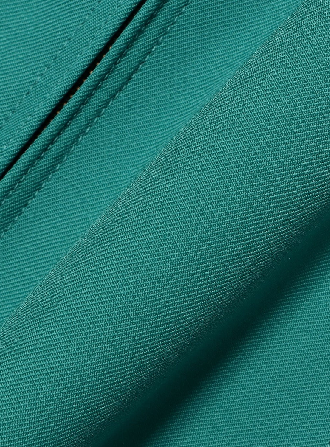 Close-up of the teal green wool gabardine fabric of the BEAMS Gabardine Zip Blouson, showing a visible twill weave and a stitched seam.